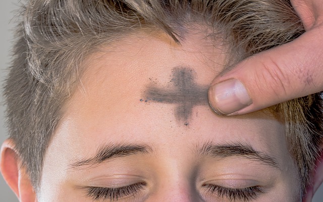 a person's forehead is marked with a cross using ash