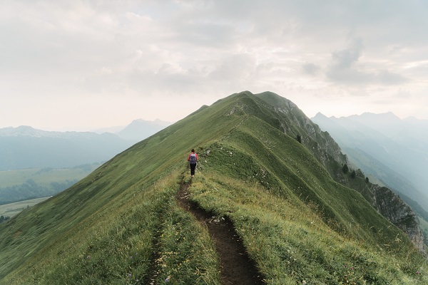 a young woman hikes along a grassy ridge in the Swiss Alps