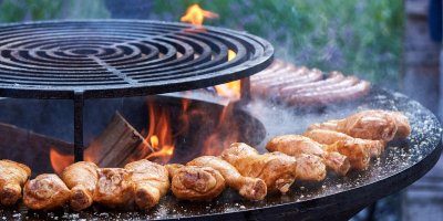 chicken and sausage cooking on a circular barbecue