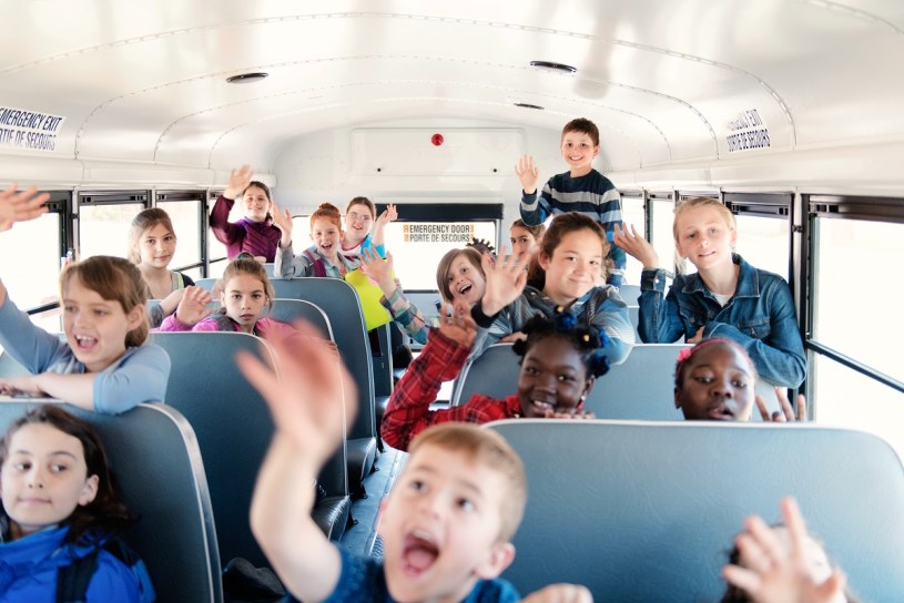 kids smiling and waving on a school bus