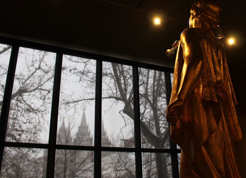 An Angel Moroni statue on display indoors looks out the window toward the Salt Lake Temple