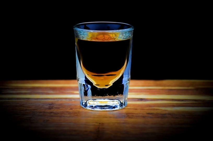 A shot glass filled with whisky and sitting on a bar
