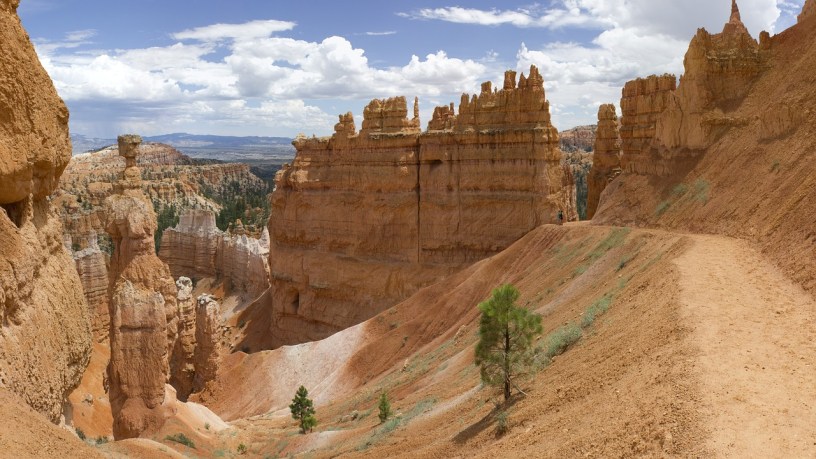 A wilderness setting on a sunny day in Bryce Canyon, Utah, with a high desert trail descending through towering rock formations