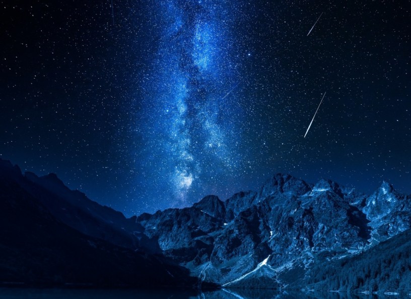 meteors falling over a rocky mountain range backed by the Milky Way