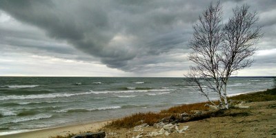 A low, dark gray cloud bank rolls over the north coast of Lake Michigan, as seen from the shore of the Upper Peninsula