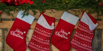 red stockings with the message "Merry Christmas," hanging from a wooden wall beneath holly