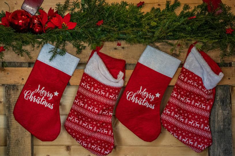 red stockings with the message "Merry Christmas," hanging from a wooden wall beneath holly
