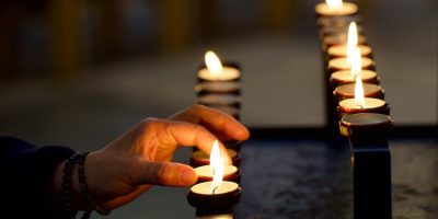 A hand is seen placing a lit votive candle on display at a church