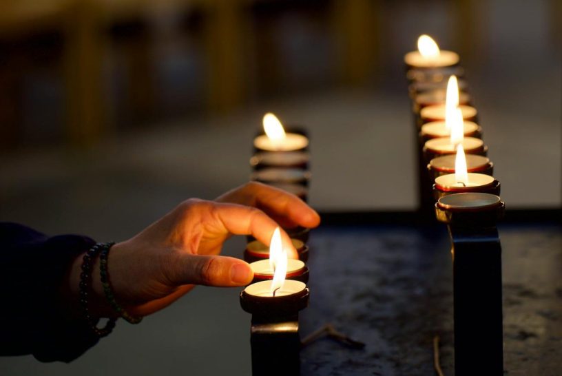 A hand is seen placing a lit votive candle on display at a church