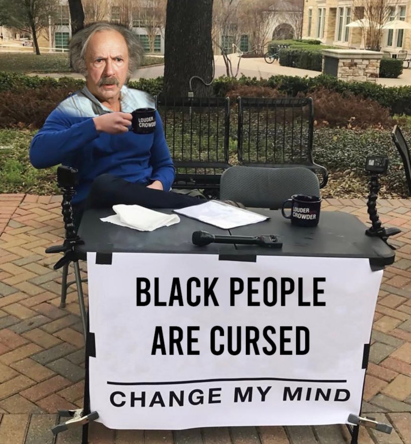 This is a manipulated photo of a classic Steven Crowder meme. Steven Crowder's face has been replaced with the wild, slightly confused expression of "Grandpa Joe". Grandpa Joe sits at a table in a public space with a sign that says, "Black people are cursed - Change my mind"